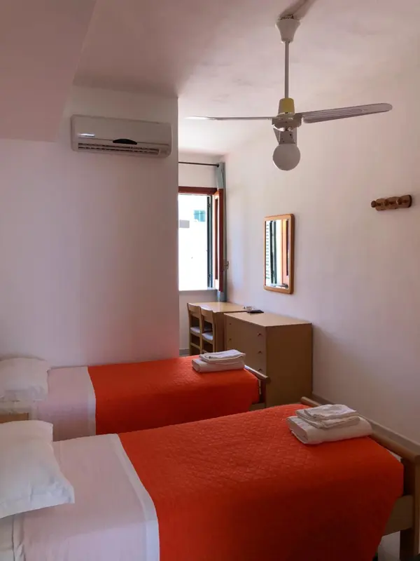 Une chambre lumineuse avec deux lits simples et un ventilateur au plafond.