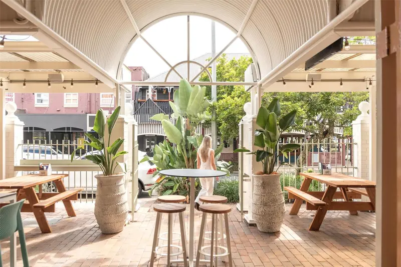 Terrasse ombragée avec tables et plantes tropicales.