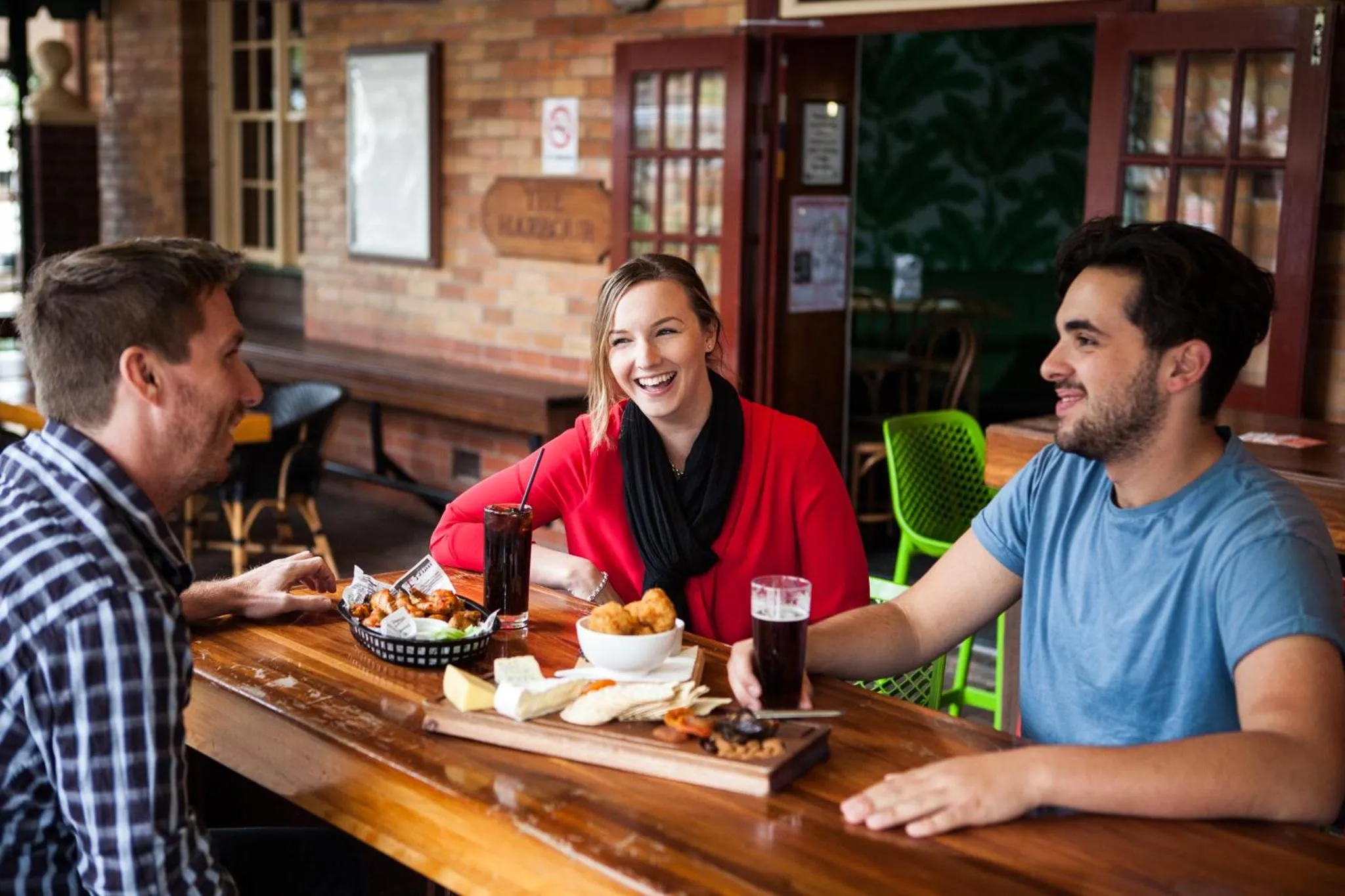 Trois personnes sourient autour d'une table en bois servant des collations et des boissons.