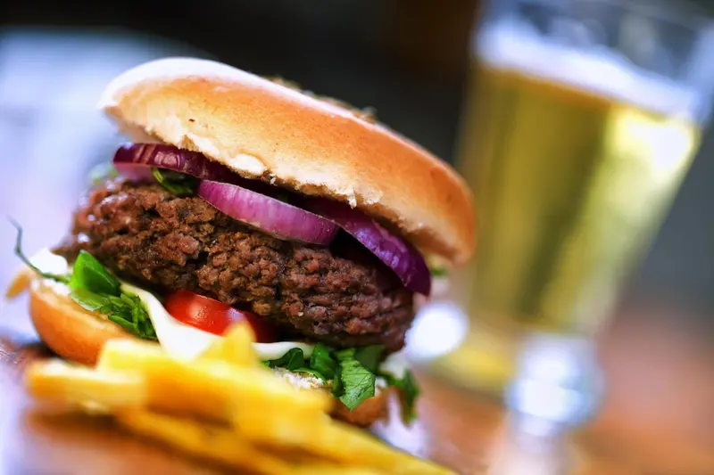 Un hamburger dégoulinant de sauce est présenté avec des frites et une bière fraîche.