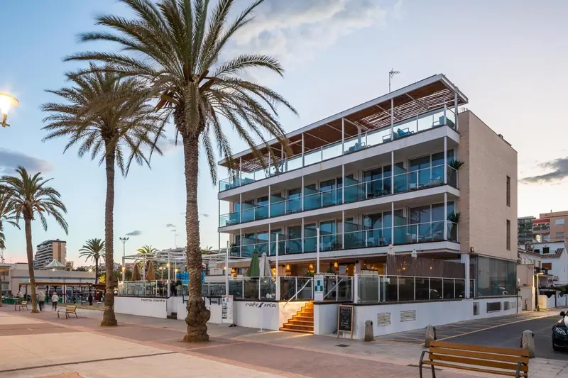 Bâtiment moderne avec des palmiers et une promenade en bord de mer au coucher du soleil.