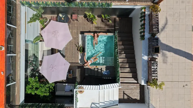 Vue aérienne d'une piscine rectangulaire entourée d'une terrasse en bois et de végétation.