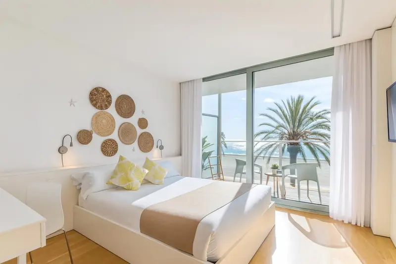 Chambre lumineuse avec un grand lit et une vue sur la mer depuis un balcon.