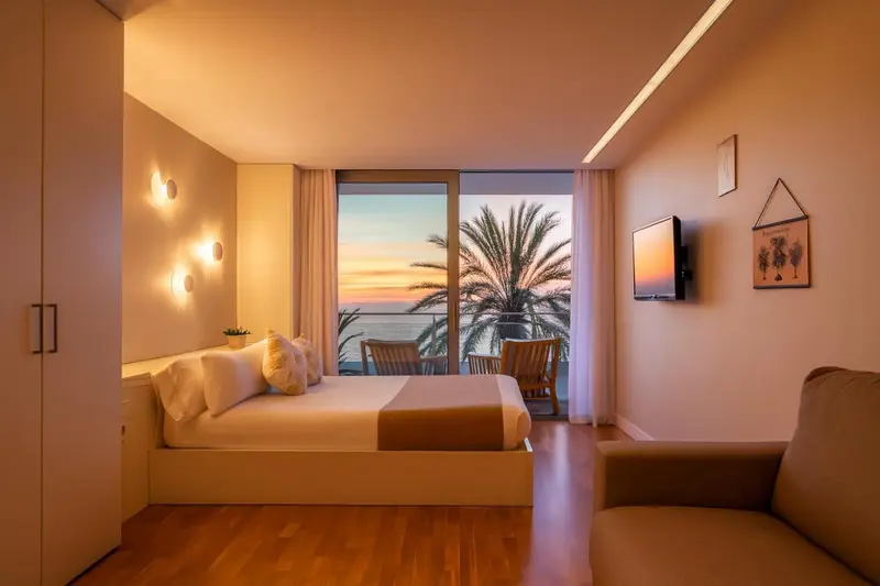 Une chambre lumineuse avec un grand lit et une vue sur la mer au coucher du soleil.