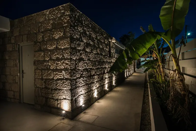 Allée illuminée le long d'un mur en pierre et de plantes tropicales.