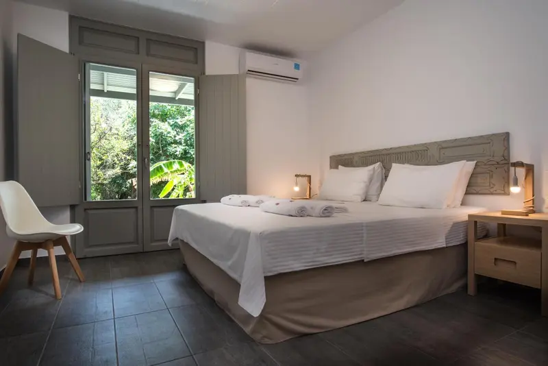 Une chambre lumineuse avec un grand lit et une fenêtre ouverte sur la végétation.