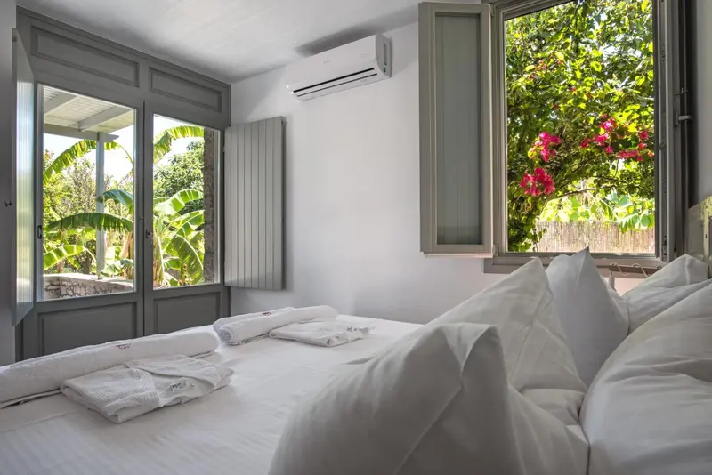 Une chambre lumineuse avec un lit fait et une vue sur une végétation luxuriante.