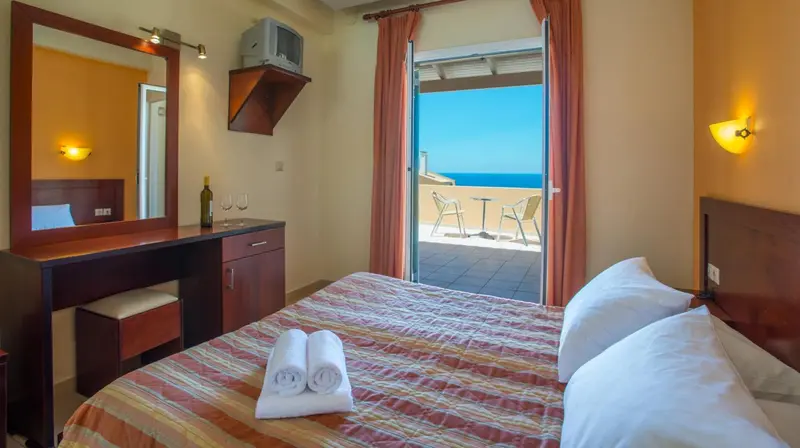 Une chambre avec un lit et un bureau donnant sur une terrasse ensoleillée.