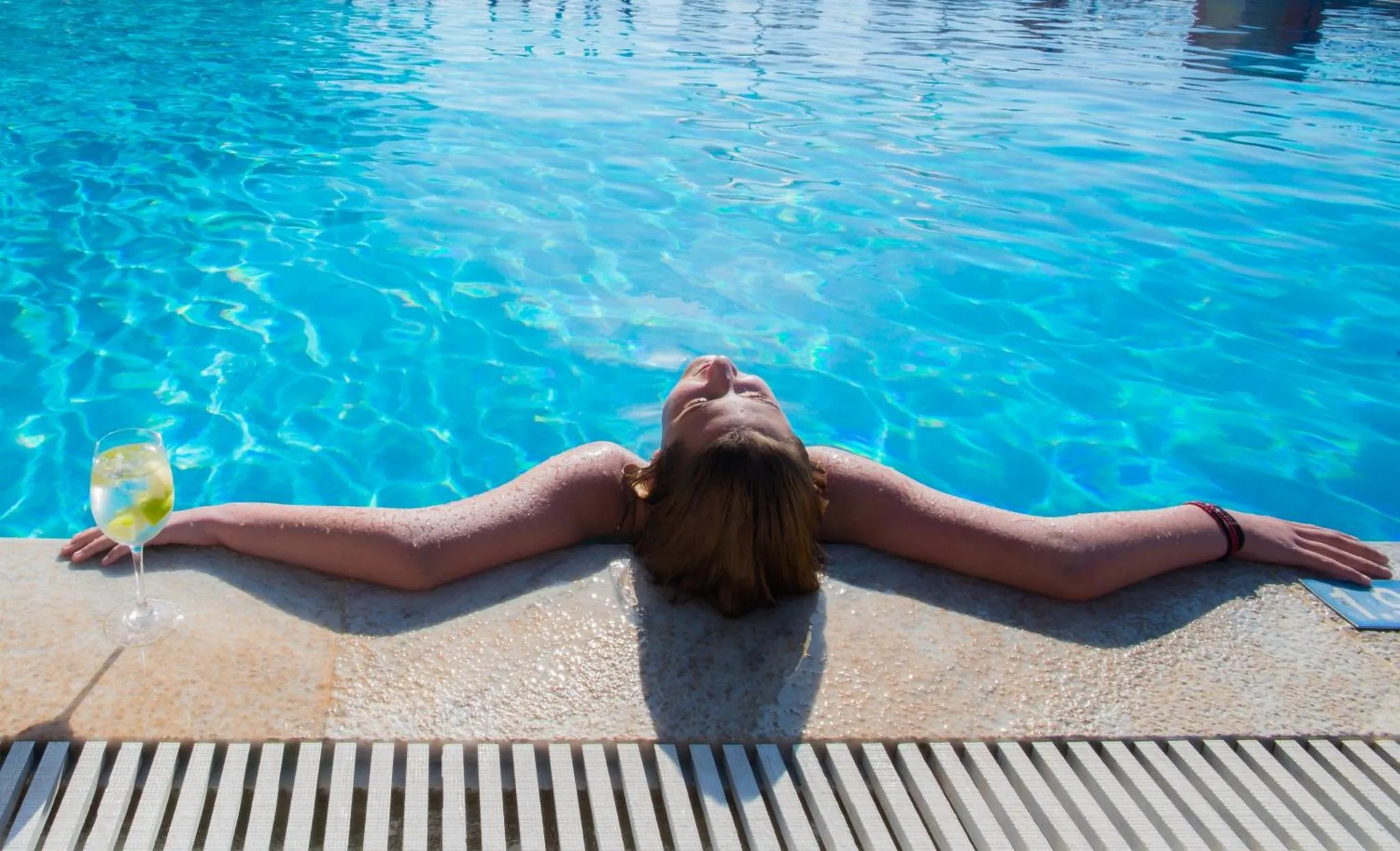 Une personne se détend au bord d'une piscine avec un verre.