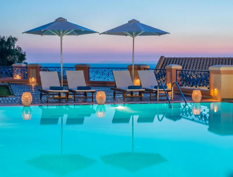 Transats et parasols bordent une piscine illuminée au crépuscule.
