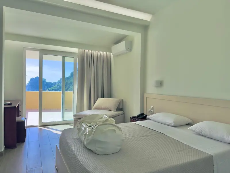 Chambre lumineuse avec un grand lit et une vue sur la mer depuis une terrasse.