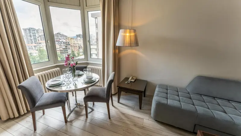 Une table ronde et des chaises sont placées devant une grande fenêtre avec vue sur la ville.