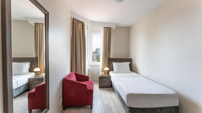 Chambre lumineuse avec deux lits simples et un fauteuil rouge.