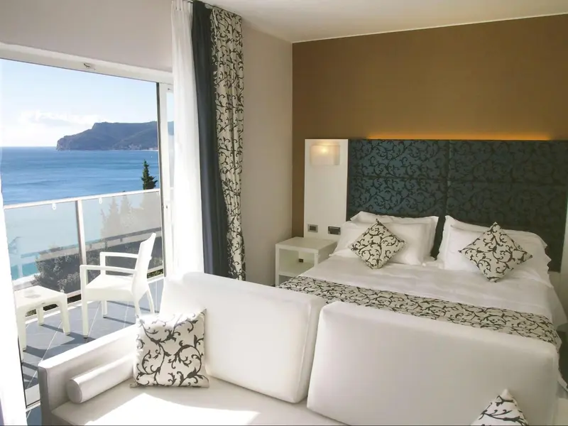 Chambre lumineuse avec un grand lit et une vue sur la mer depuis un balcon.
