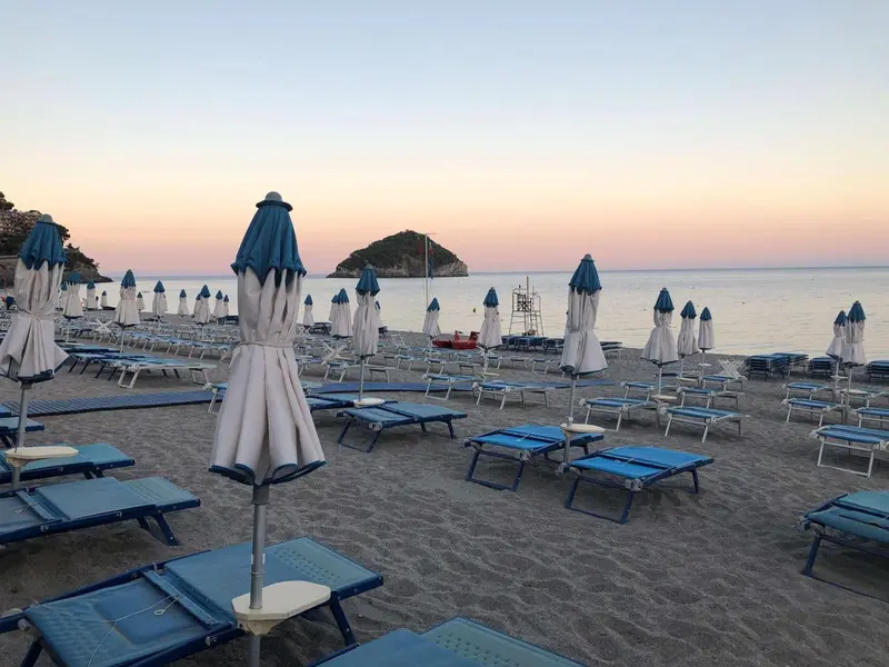 Transats bleus et parasols blancs sur une plage de sable fin au coucher du soleil.