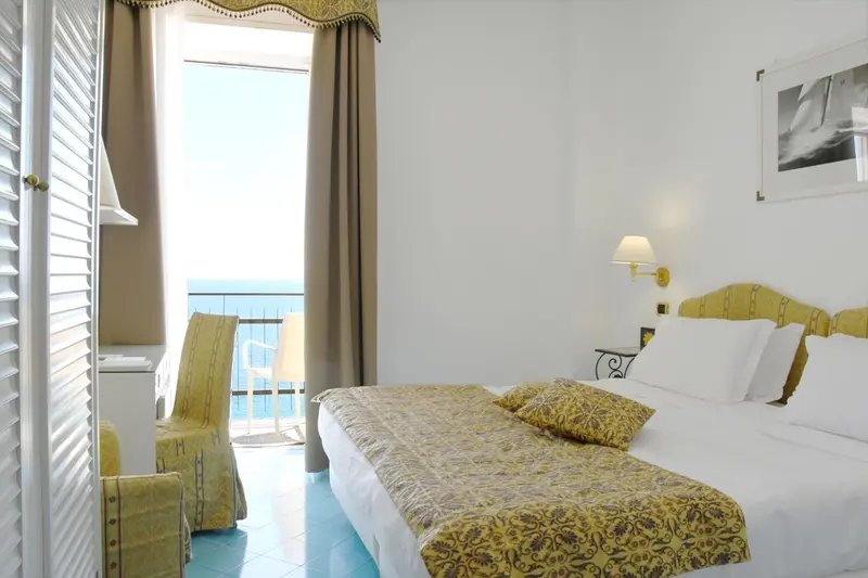 Une chambre lumineuse avec un lit fait et un balcon donnant sur la mer.