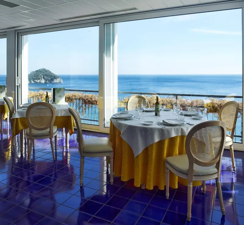 Une salle lumineuse avec des tables dressées face à une vue sur la mer.