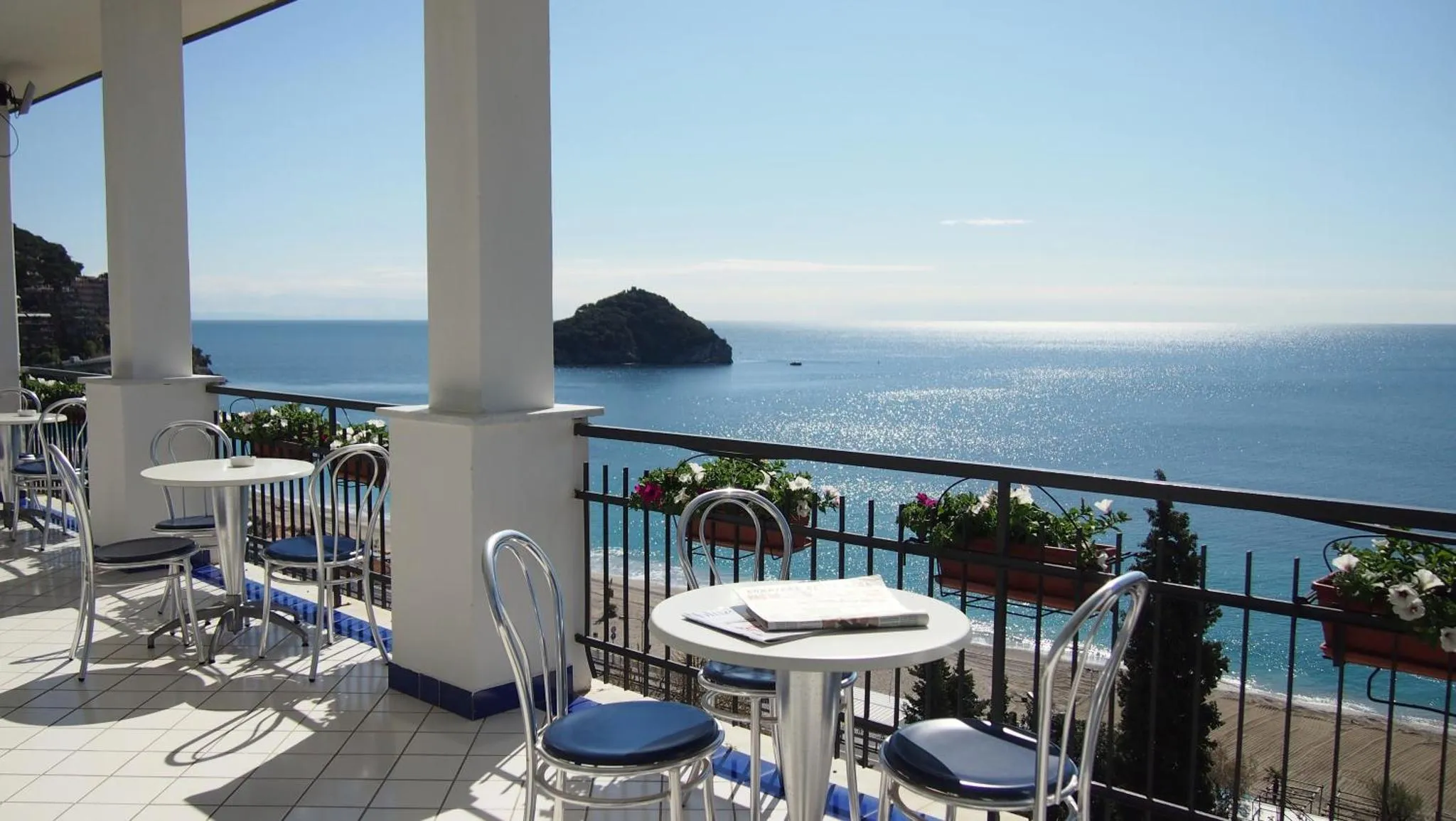 Terrasse avec tables et chaises donnant sur la mer et une île.