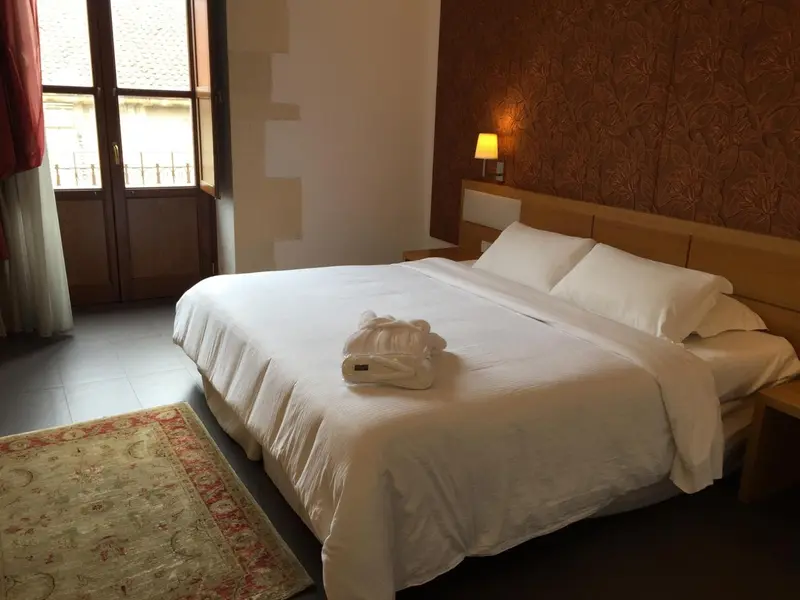 Une chambre lumineuse avec un grand lit recouvert de draps blancs et un tapis oriental.