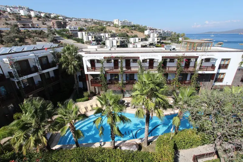 Vue aérienne d'un complexe hôtelier blanc avec une piscine et des palmiers.
