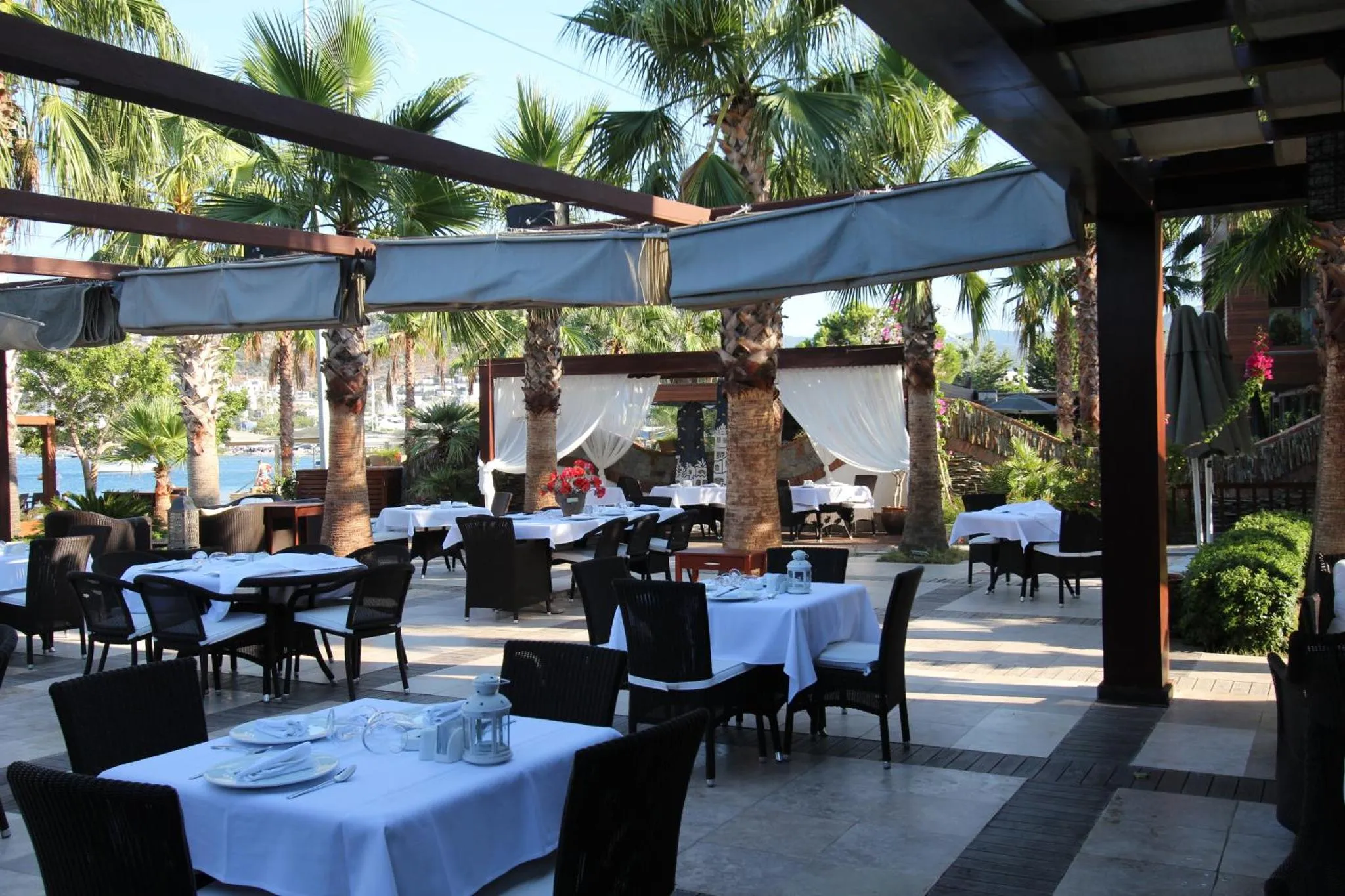 Terrasse ombragée avec tables nappées face à la mer.