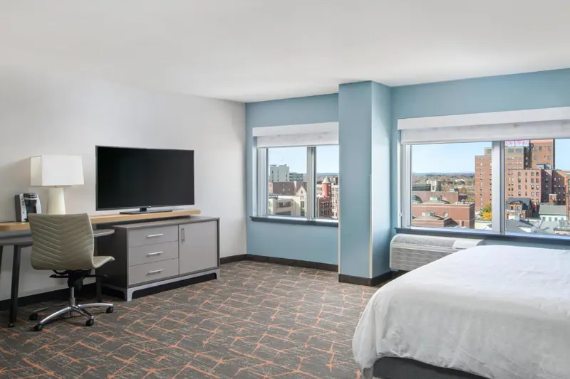 Une chambre d'hôtel lumineuse avec un bureau et une vue sur la ville.