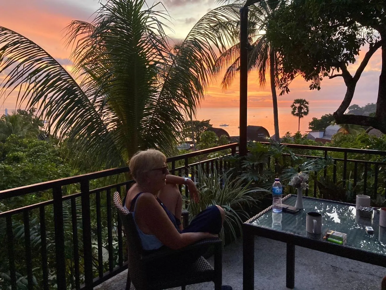 Une personne est assise à une table sur une terrasse avec vue sur la mer au coucher du soleil.