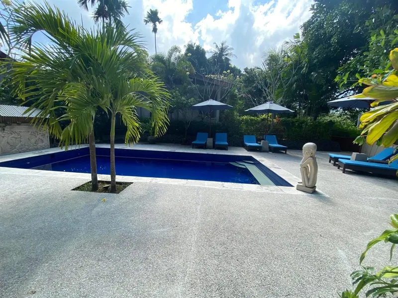 Piscine rectangulaire entourée d'une terrasse ensoleillée avec des transats bleus.
