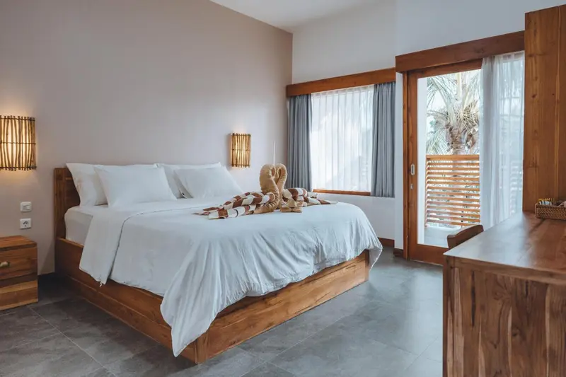 Une chambre lumineuse avec un grand lit recouvert de draps blancs et une terrasse en bois.