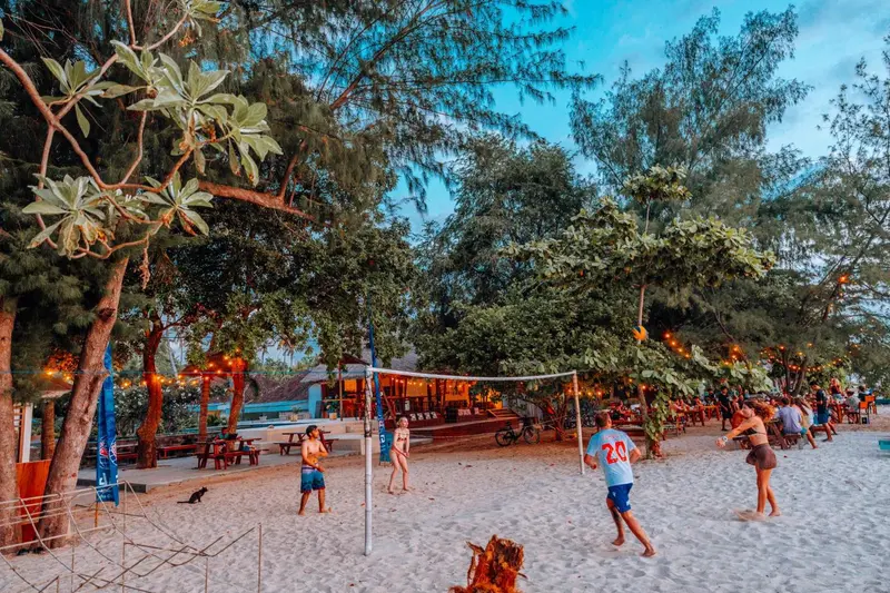 Une plage de sable clair avec des personnes jouant au volleyball au coucher du soleil.