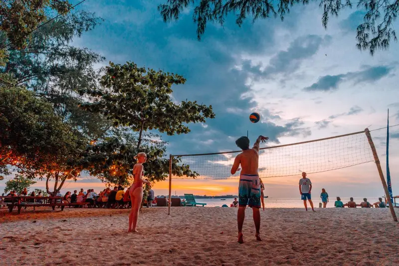 Des personnes jouent au volley-ball sur une plage de sable au coucher du soleil.
