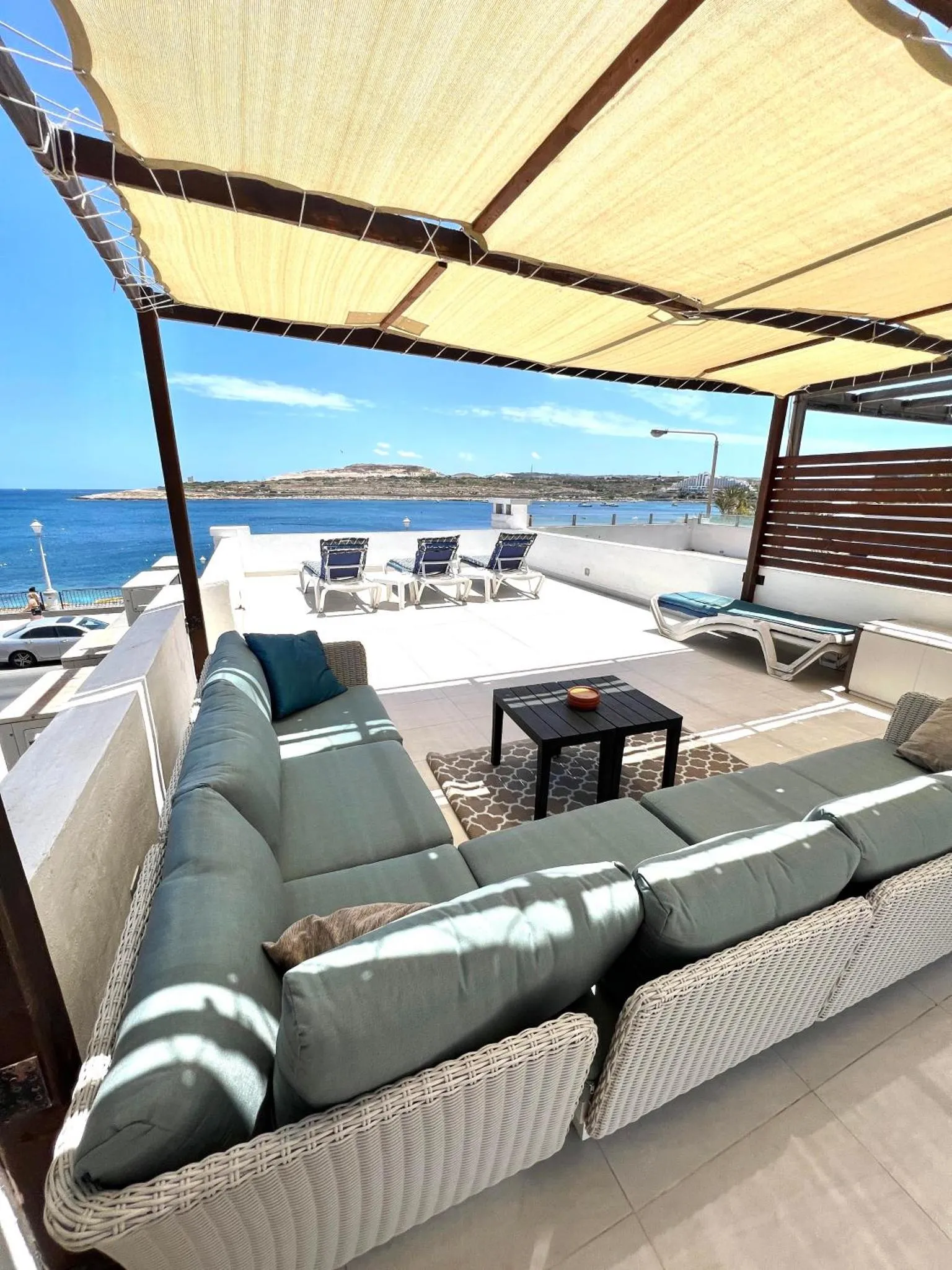 Espace de détente extérieur avec canapés et transats face à la mer.