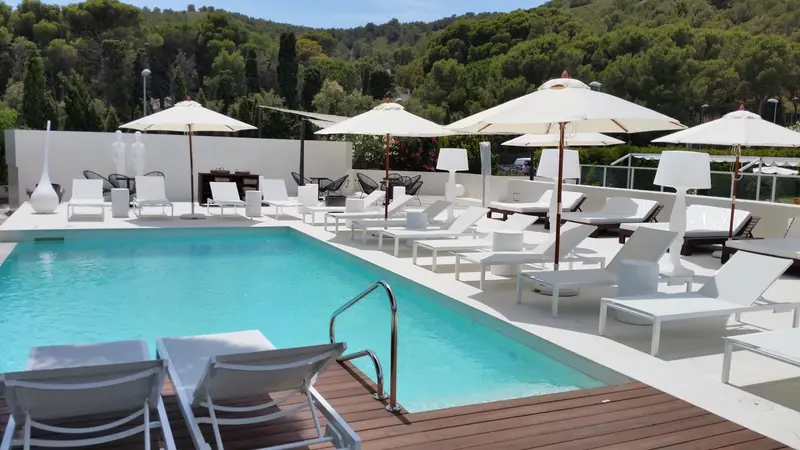 Transats blancs disposés autour d'une piscine rectangulaire ensoleillée.
