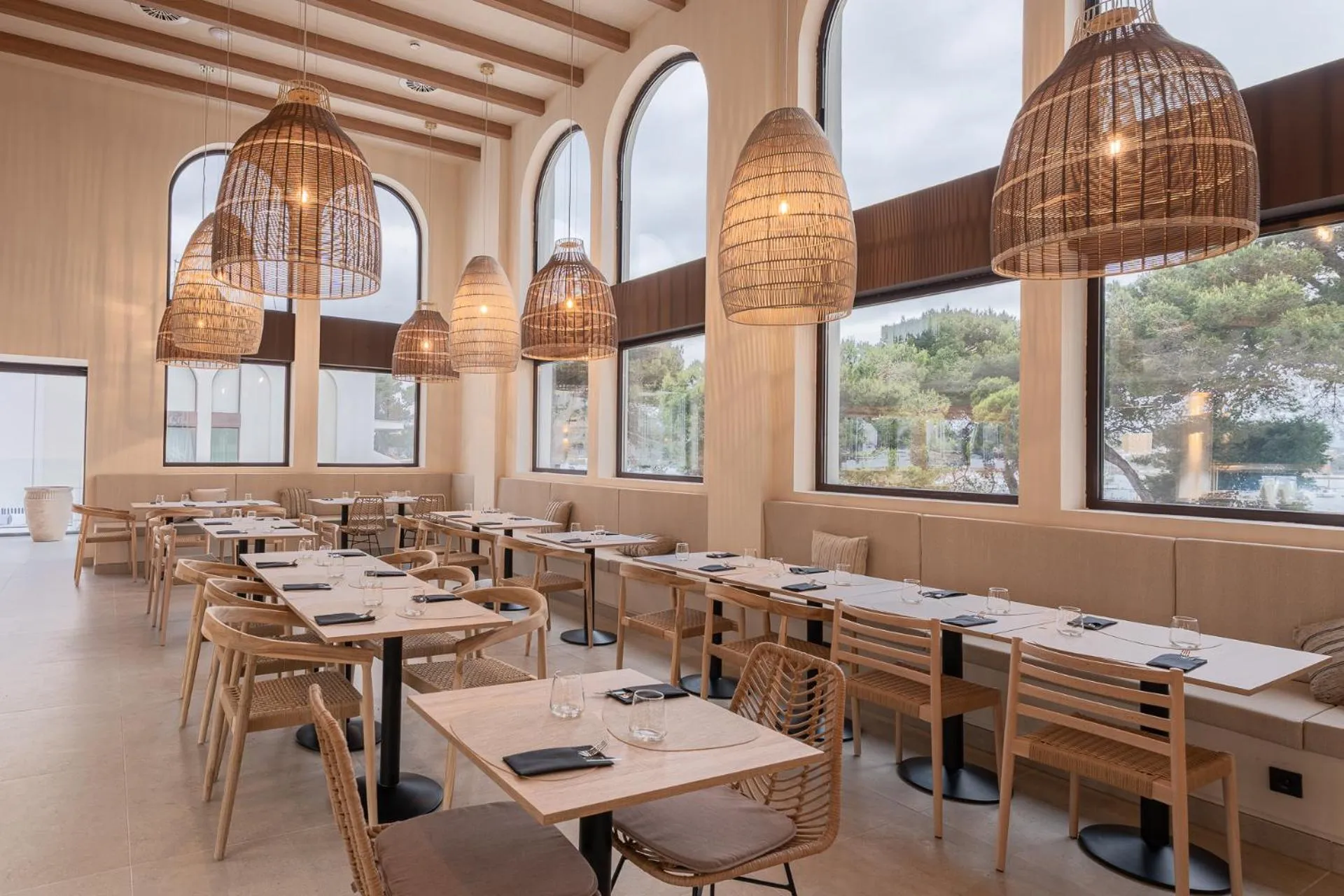Une salle lumineuse avec des tables et des chaises en bois, éclairée par des suspensions en osier.