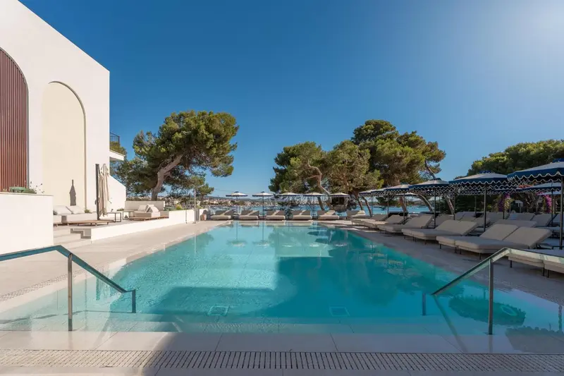 Une piscine rectangulaire bordée de transats sous le soleil.