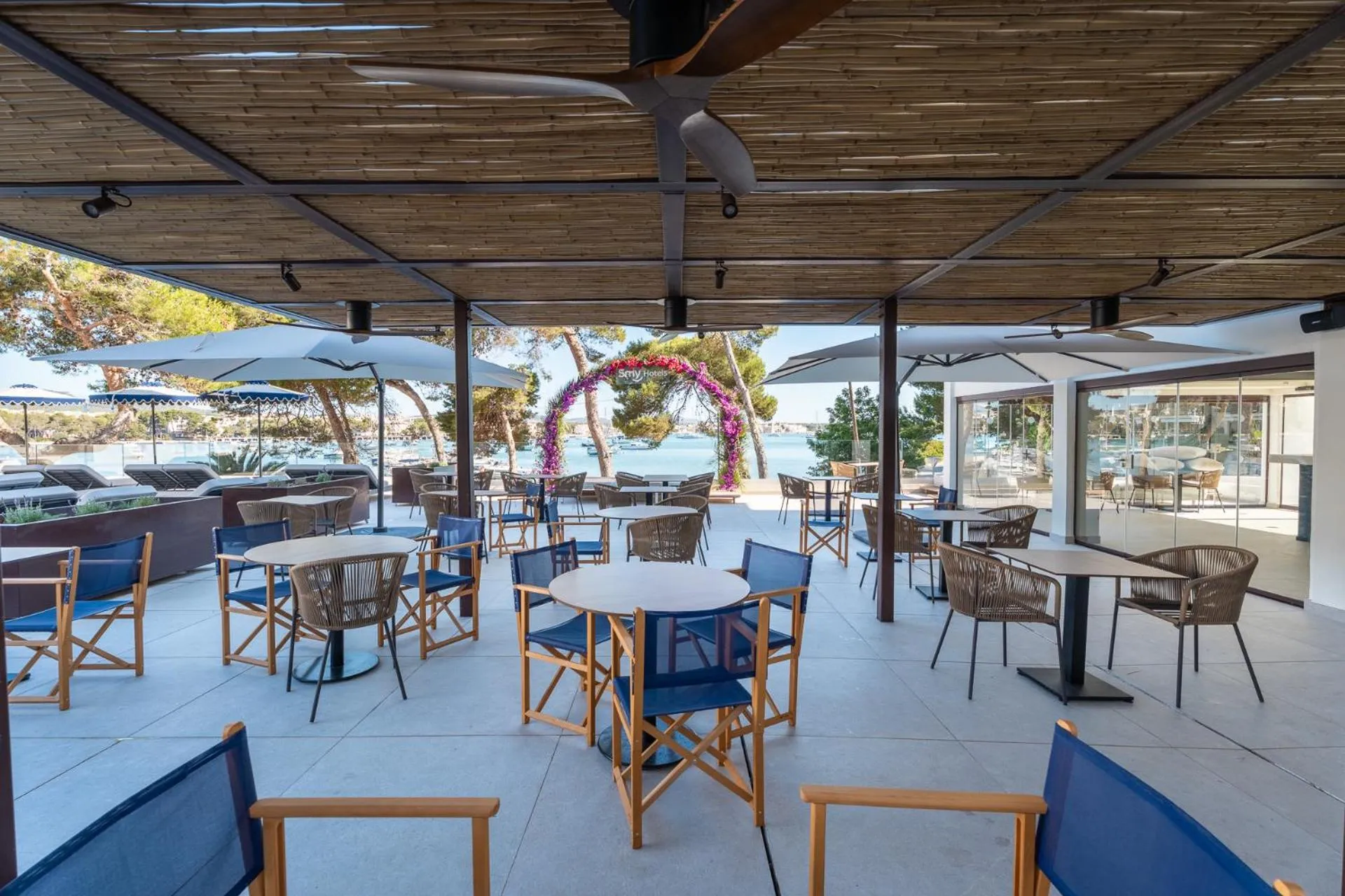 Terrasse ombragée avec tables et chaises face à la mer.