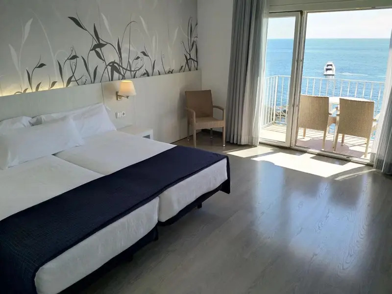 Une chambre lumineuse avec un lit double et un accès à une terrasse ensoleillée.