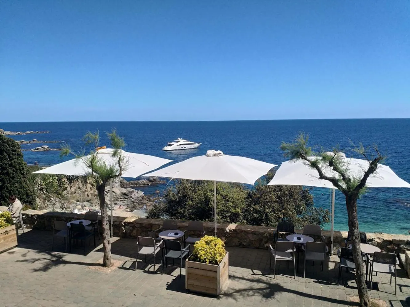 Terrasse ombragée avec tables et chaises donnant sur la mer.