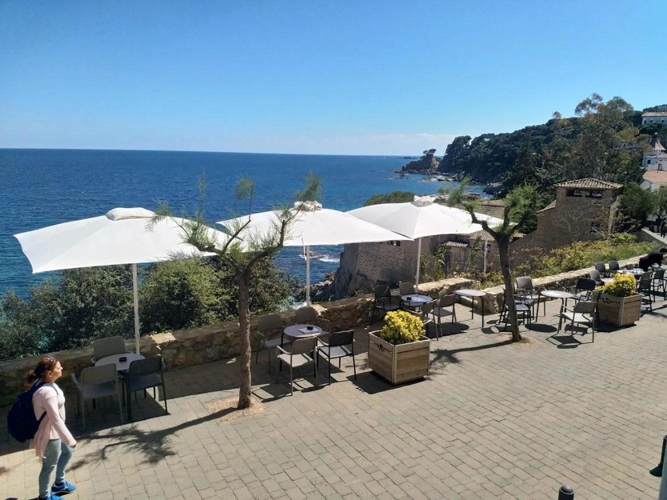 Terrasse ombragée avec tables et chaises surplombant la mer.