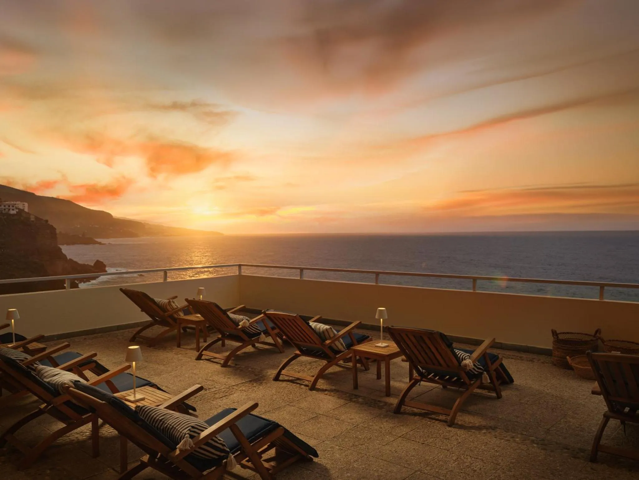 Transats alignés sur une terrasse face à la mer au coucher du soleil.