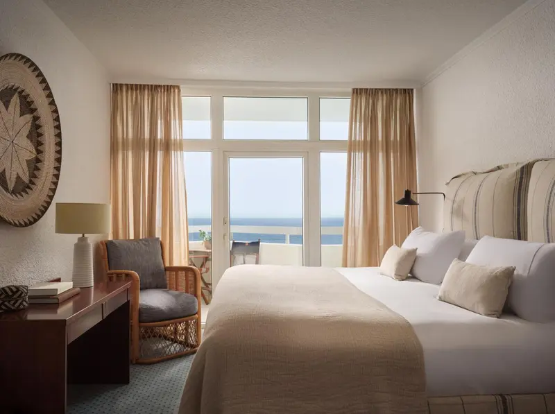 Chambre lumineuse avec un lit fait et une vue sur la mer.
