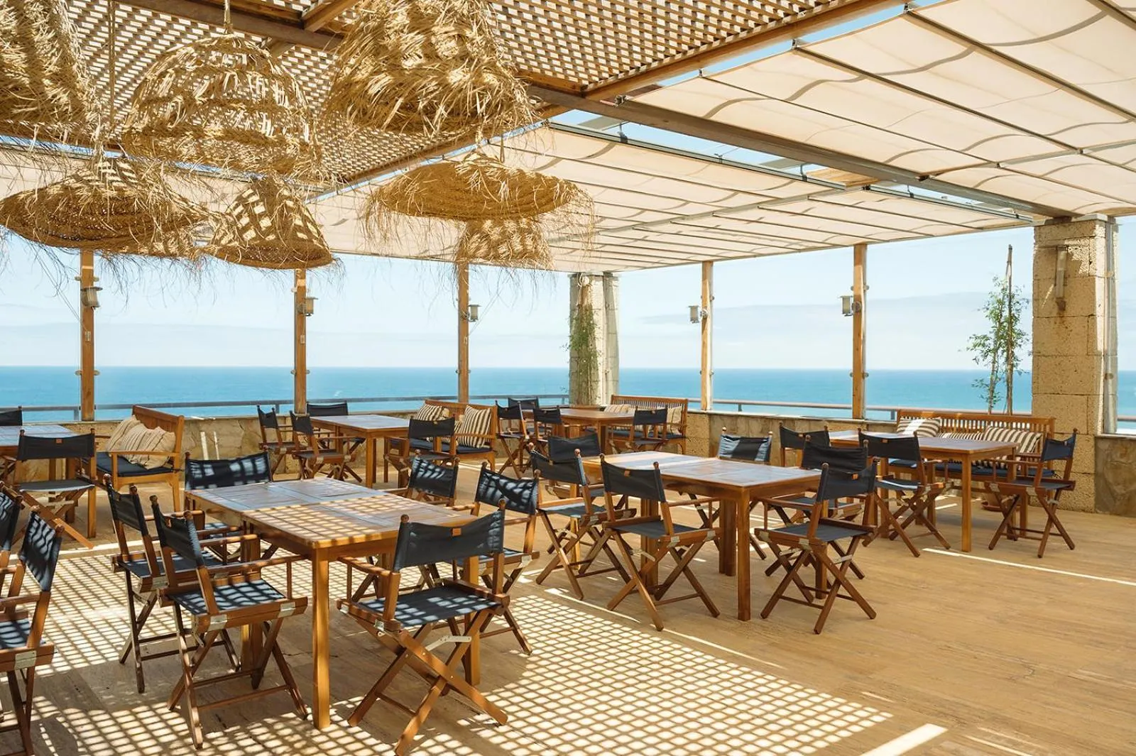 Terrasse ombragée avec tables et chaises donnant sur la mer.
