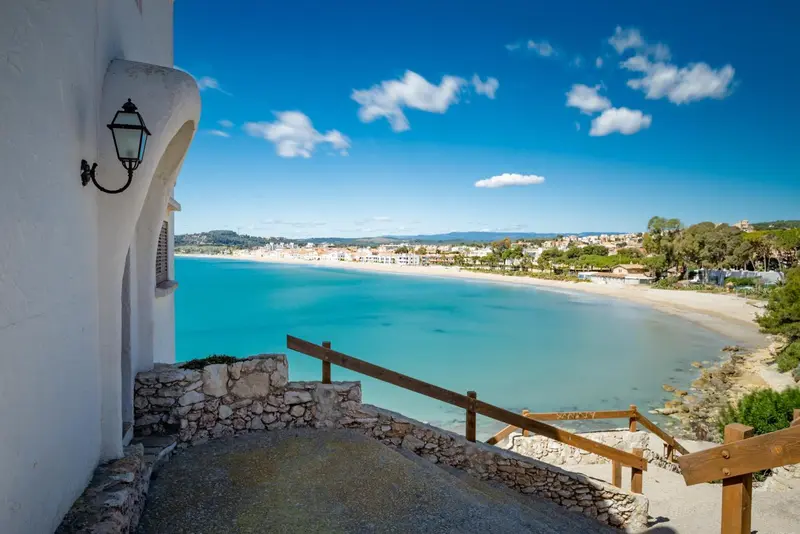 Vue sur une plage de sable fin et une mer turquoise depuis un escalier en pierre.