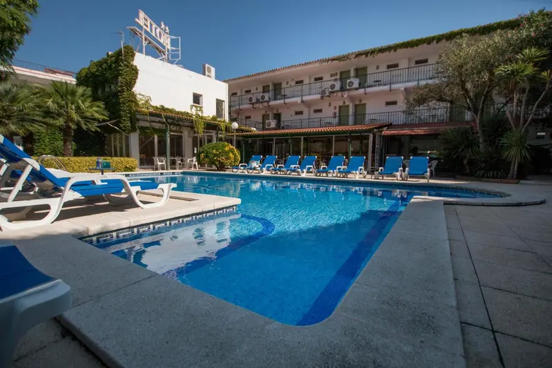 Une piscine turquoise bordée de chaises longues bleues devant un bâtiment blanc.