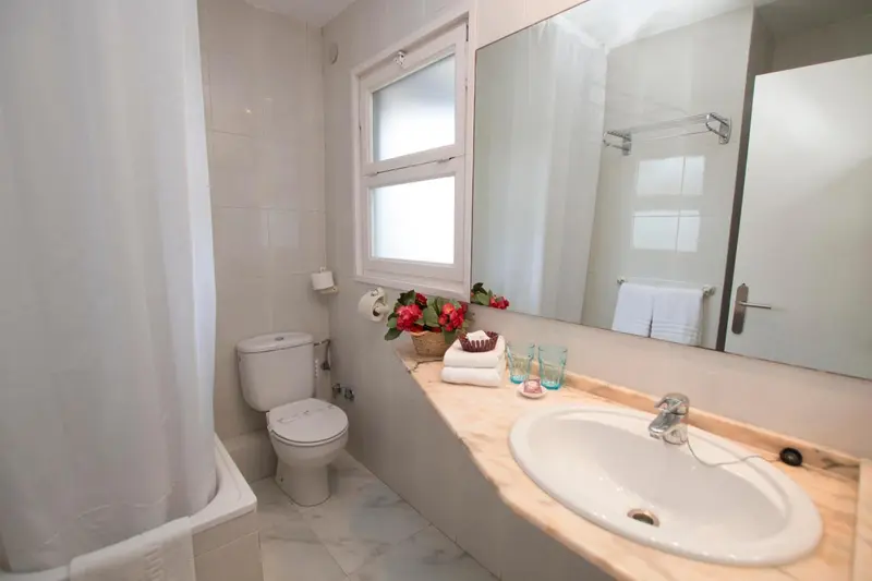 Une salle de bain lumineuse avec douche, lavabo et toilettes.
