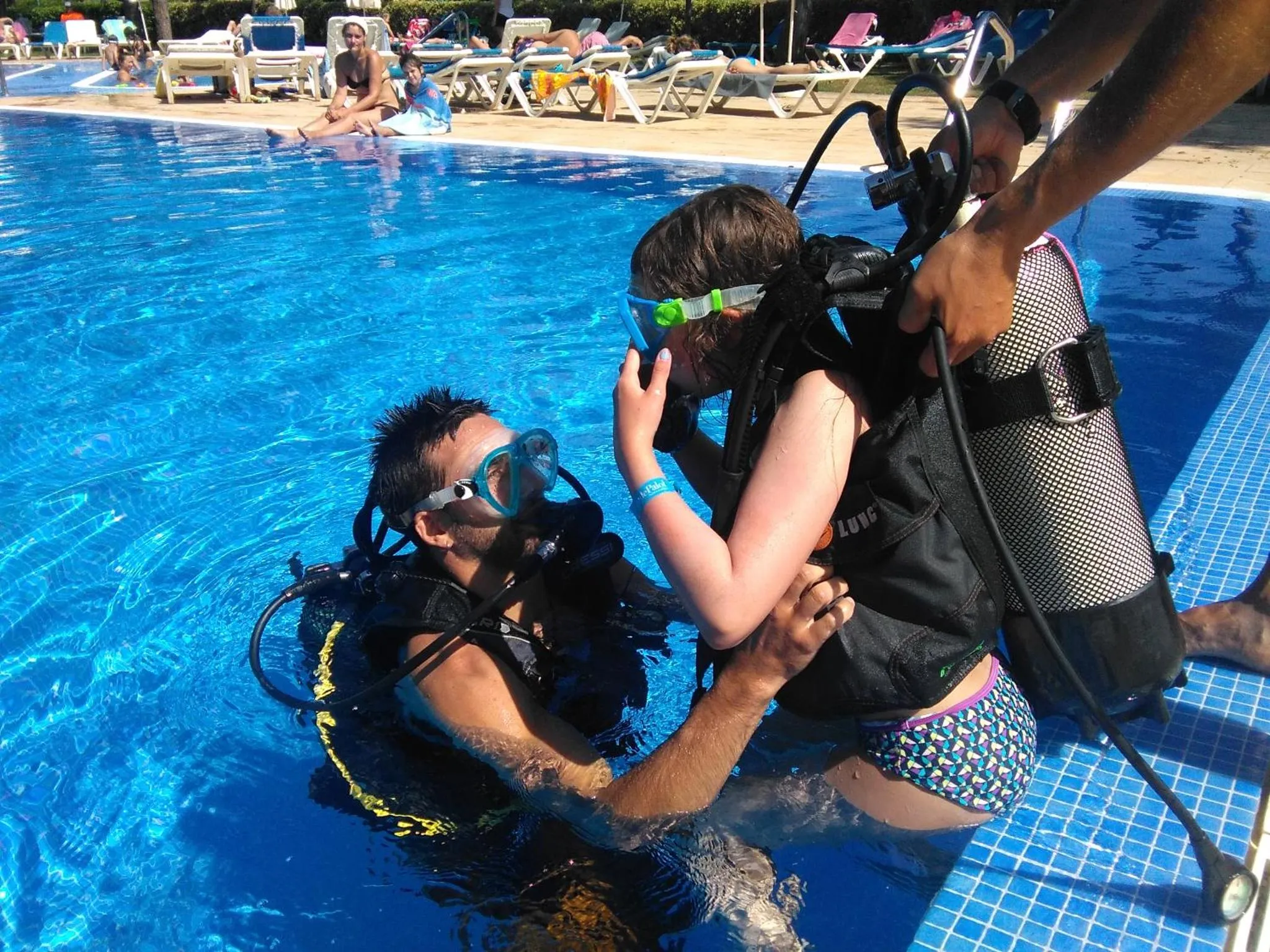 Une personne aide une autre à mettre un équipement de plongée au bord d'une piscine.
