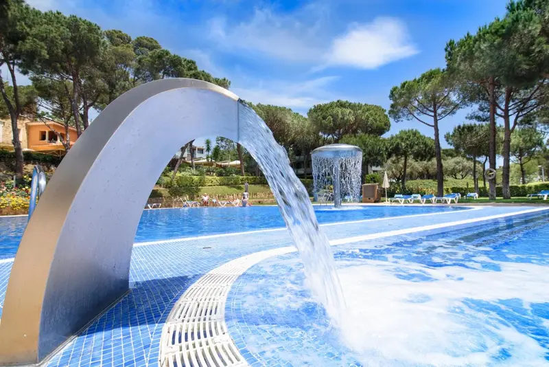 Une cascade d'eau artificielle se déverse dans une piscine bleue entourée de végétation luxuriante.