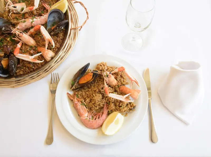 Assiette de paella aux fruits de mer, accompagnée d'un verre de vin et de couverts.