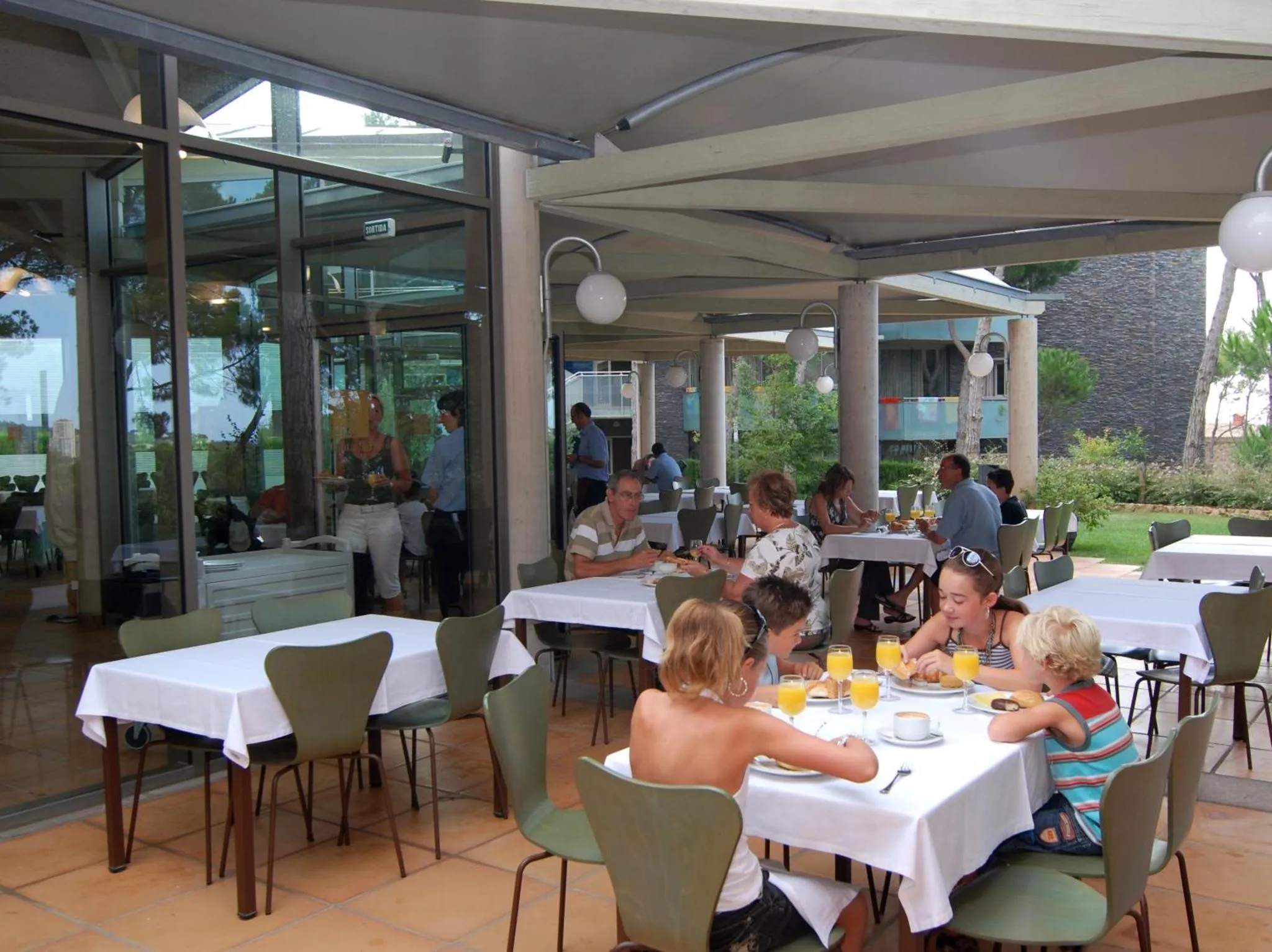 Une terrasse ombragée avec des tables et des chaises où des clients prennent leur repas.