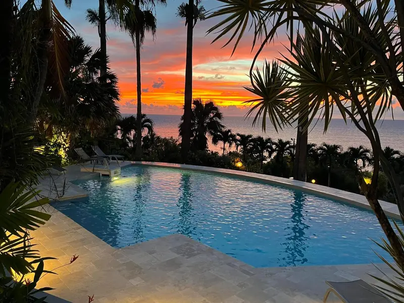 Une piscine bordée d'une terrasse avec vue sur la mer au coucher du soleil.